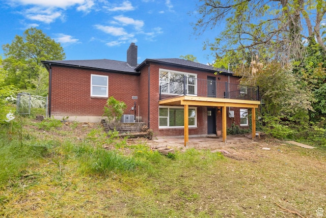 rear view of property with a chimney, brick siding, a patio, central AC unit, and a deck
