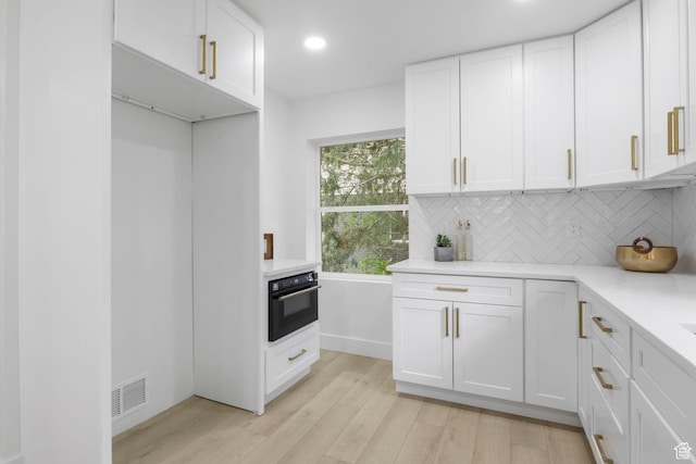 kitchen with light wood-style flooring, black oven, visible vents, light countertops, and decorative backsplash