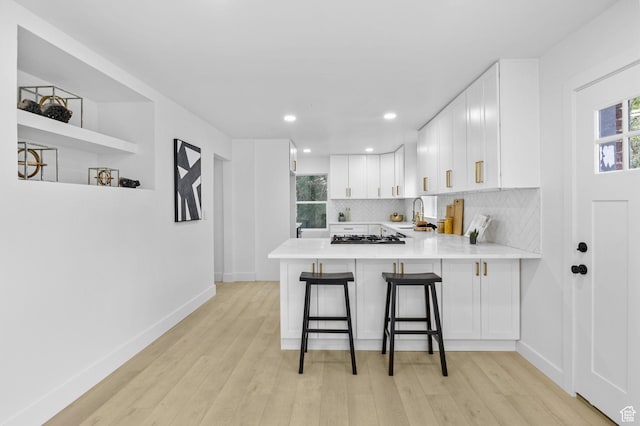 kitchen featuring light wood finished floors, tasteful backsplash, light countertops, and baseboards