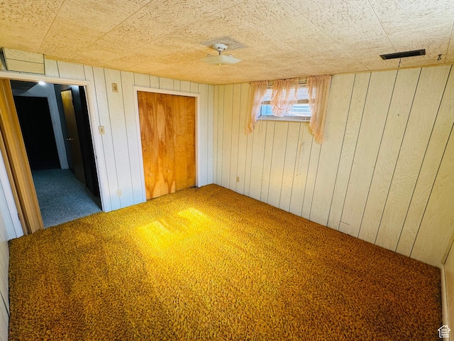 unfurnished bedroom featuring carpet, wood walls, and a closet