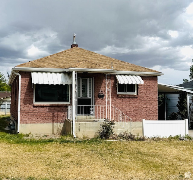 back of property featuring a lawn, roof with shingles, brick siding, and a chimney