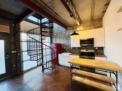 kitchen with concrete floors, a sink, stainless steel appliances, white cabinetry, and backsplash