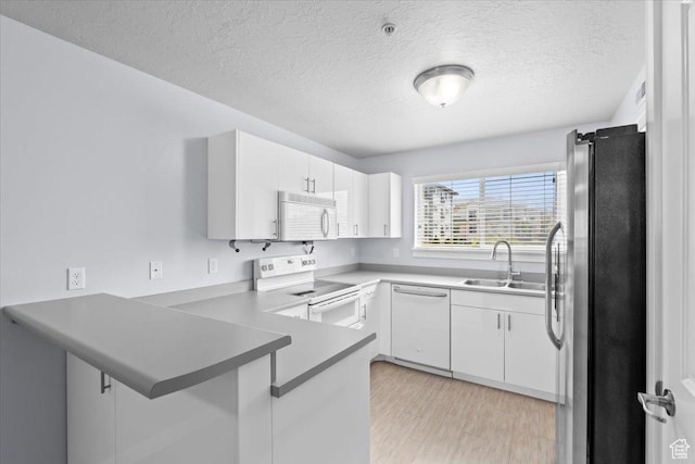 kitchen with a sink, a peninsula, white appliances, a textured ceiling, and white cabinets