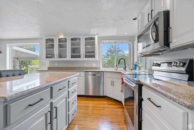 3470 W Maynard Ct, Riverton, UT 84065 - kitchen with light wood-style flooring, a textured ceiling, glass insert cabinets, a sink, and appliances with stainless steel finishes