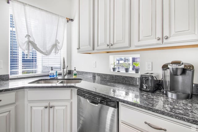 kitchen with white cabinetry, a sink, stainless steel dishwasher, and dark stone counters