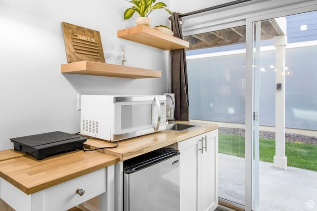 interior space with wooden counters, refrigerator, open shelves, white cabinetry, and white microwave
