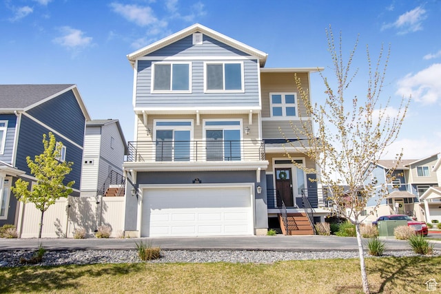 view of front of house featuring driveway, an attached garage, fence, and a balcony