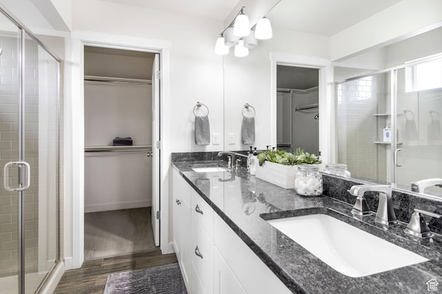 bathroom with a sink, a walk in closet, a stall shower, and wood finished floors