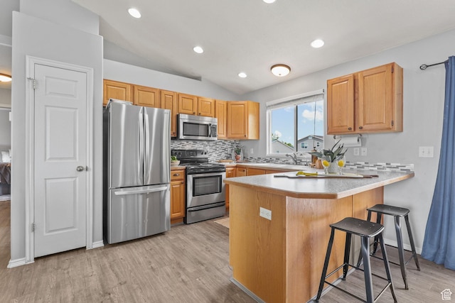 kitchen with a peninsula, light wood-style flooring, appliances with stainless steel finishes, decorative backsplash, and lofted ceiling