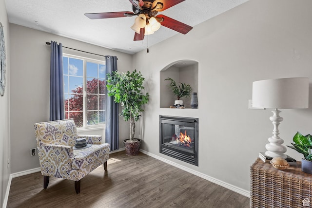 living area with wood finished floors, baseboards, ceiling fan, and a glass covered fireplace
