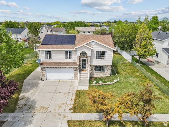 raised ranch with driveway, a garage, a residential view, a front yard, and roof mounted solar panels