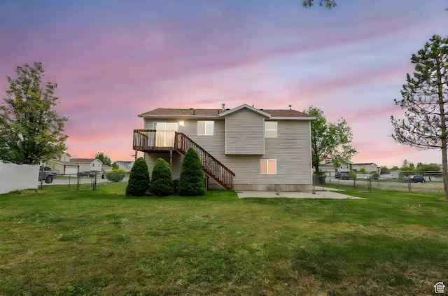 back of house at dusk with a yard, stairway, a deck, and a fenced backyard