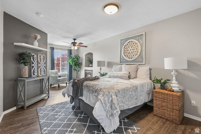 bedroom with a ceiling fan, a textured ceiling, baseboards, wood finished floors, and arched walkways