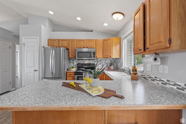 kitchen with lofted ceiling, a sink, a peninsula, decorative backsplash, and stainless steel appliances