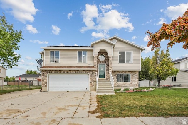 bi-level home with a garage, fence, concrete driveway, solar panels, and a front yard