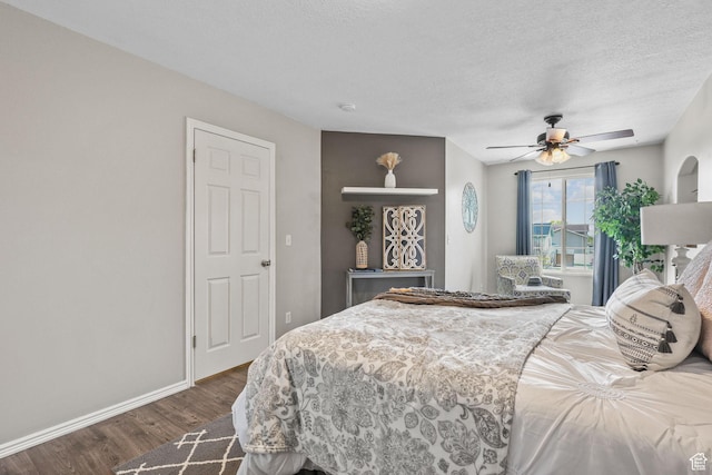 bedroom with ceiling fan, a textured ceiling, baseboards, and dark wood finished floors