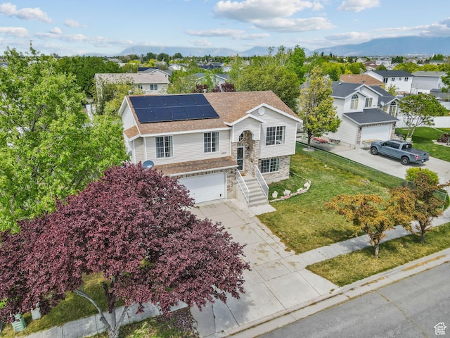 split foyer home featuring driveway, solar panels, a garage, a residential view, and stone siding