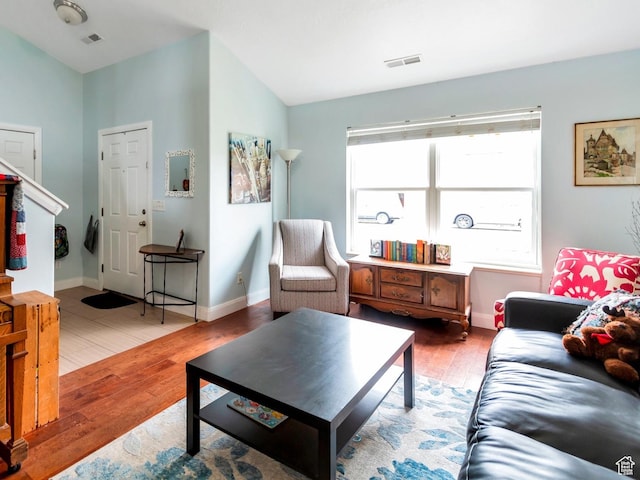 living room featuring baseboards, vaulted ceiling, visible vents, and wood finished floors