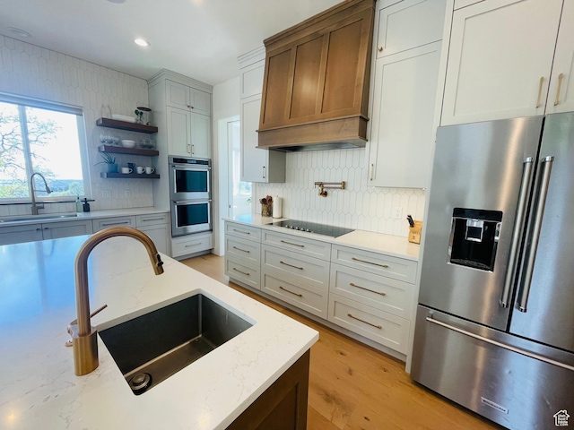 kitchen featuring decorative backsplash, premium range hood, appliances with stainless steel finishes, and a sink