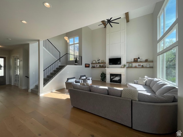 living area with wood finished floors, a ceiling fan, a high ceiling, stairway, and recessed lighting