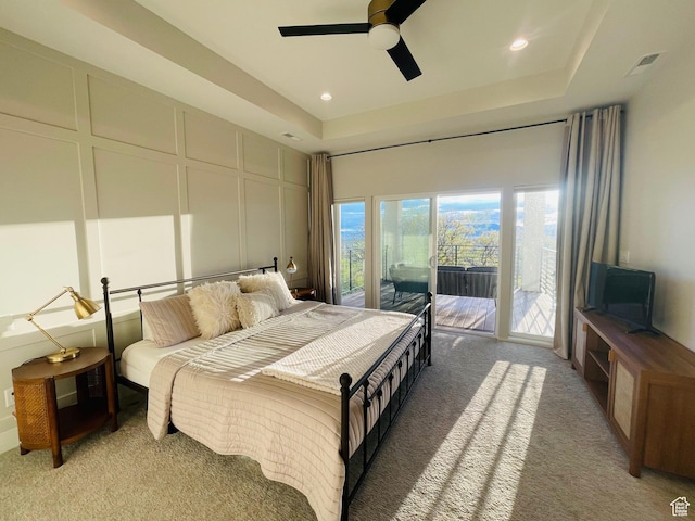 bedroom featuring access to exterior, a decorative wall, light carpet, a tray ceiling, and recessed lighting