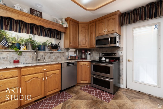 kitchen featuring brown cabinets, a sink, stainless steel appliances, tasteful backsplash, and light stone counters
