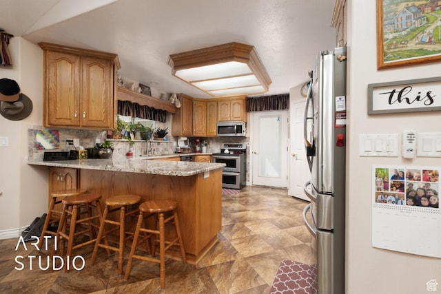 kitchen with a peninsula, stainless steel appliances, a kitchen breakfast bar, light stone countertops, and tasteful backsplash