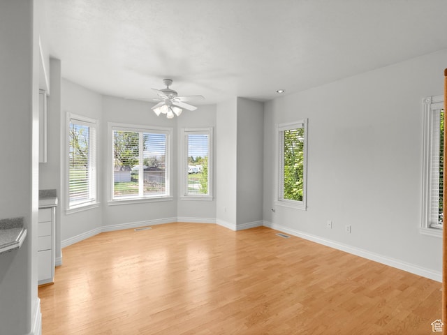 empty room featuring plenty of natural light, light wood-type flooring, baseboards, and a ceiling fan