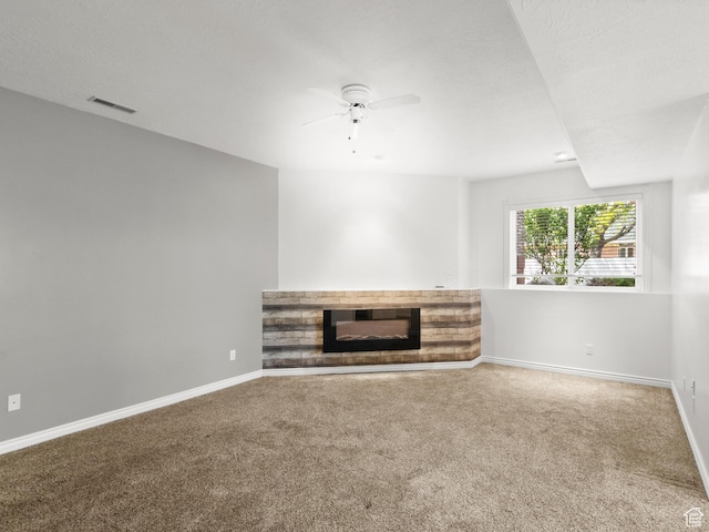 unfurnished living room featuring carpet flooring, a glass covered fireplace, a ceiling fan, and baseboards