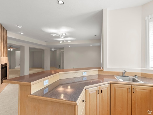 kitchen with a sink, dark countertops, a fireplace, recessed lighting, and light brown cabinetry