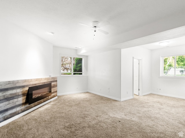unfurnished living room featuring light carpet, a glass covered fireplace, baseboards, and a ceiling fan