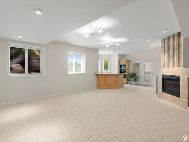unfurnished living room with a tiled fireplace, baseboards, light carpet, and recessed lighting