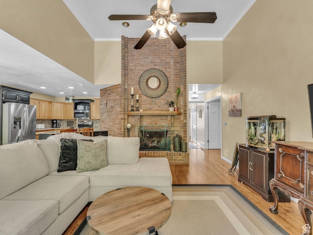 4760 S Meadow Creek Ln E, Ogden, UT 84403 - living area with a towering ceiling, light wood-style floors, a ceiling fan, a brick fireplace, and baseboards