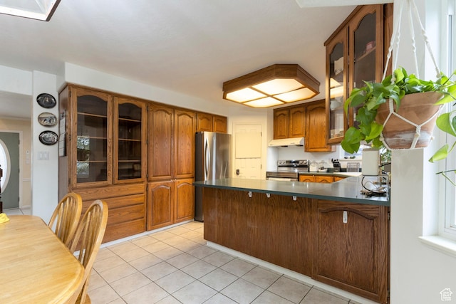 kitchen with stainless steel appliances, under cabinet range hood, a peninsula, dark countertops, and brown cabinetry