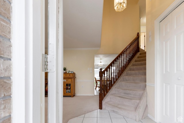stairway featuring carpet flooring, a chandelier, baseboards, crown molding, and tile patterned flooring