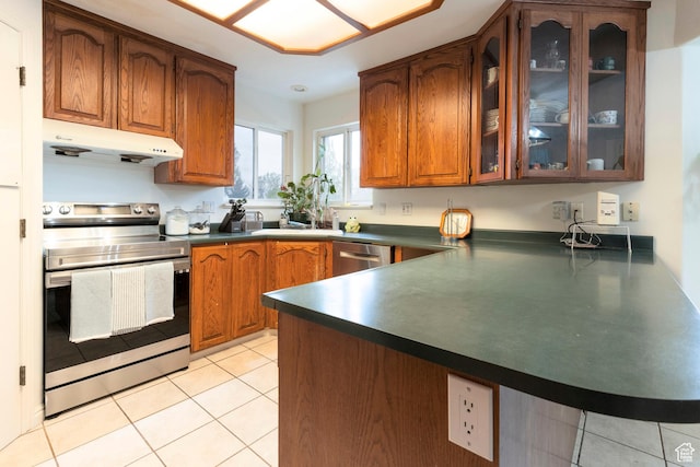 kitchen with stainless steel appliances, under cabinet range hood, a peninsula, dark countertops, and brown cabinets