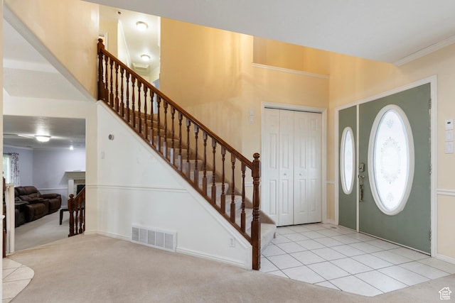 carpeted foyer with stairs, tile patterned flooring, and ornamental molding
