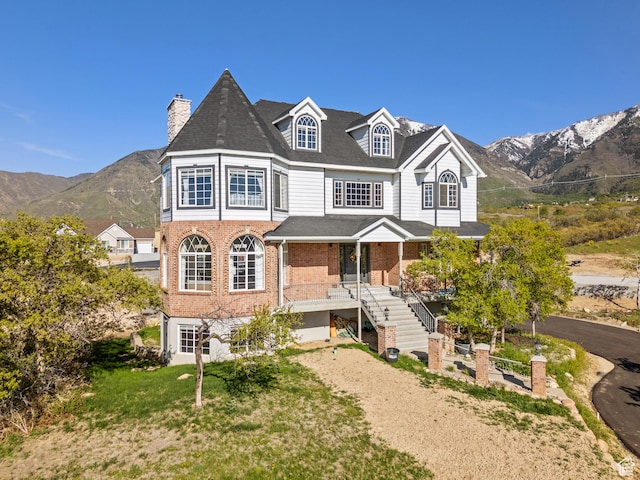 view of front of home with brick siding, a mountain view, a chimney, and stairway