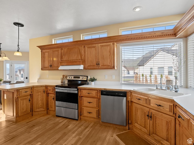 kitchen featuring stainless steel appliances, a sink, under cabinet range hood, light wood-type flooring, and a peninsula