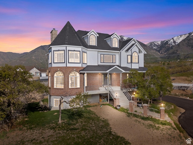 view of front of property featuring stairs, brick siding, covered porch, a chimney, and a mountain view