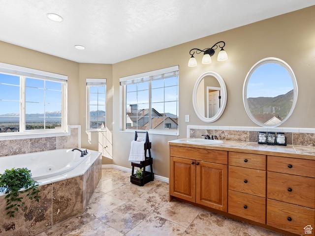 full bathroom with vanity, a tub with jets, and baseboards