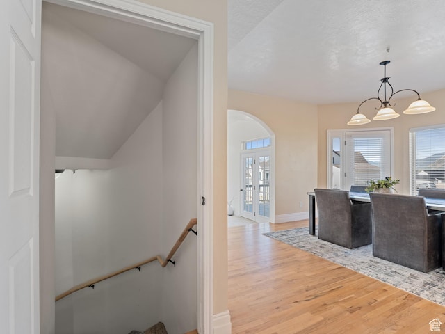 hall with light wood-style floors, an upstairs landing, a chandelier, baseboards, and french doors