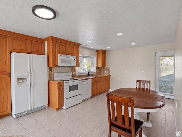 kitchen with white appliances, a sink, decorative backsplash, light tile patterned flooring, and brown cabinets