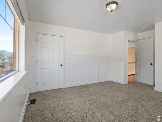 unfurnished bedroom featuring carpet, a wainscoted wall, and baseboards