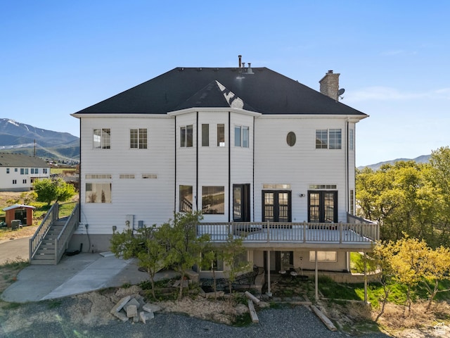 back of house featuring a deck with mountain view, a chimney, stairs, french doors, and a patio