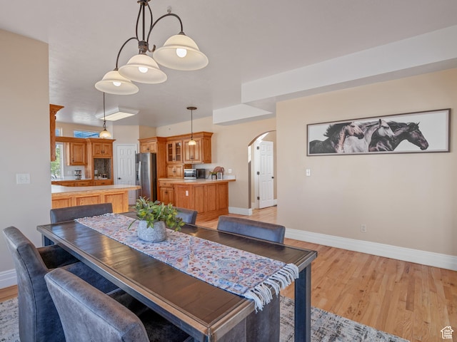 dining space with arched walkways, baseboards, and light wood finished floors