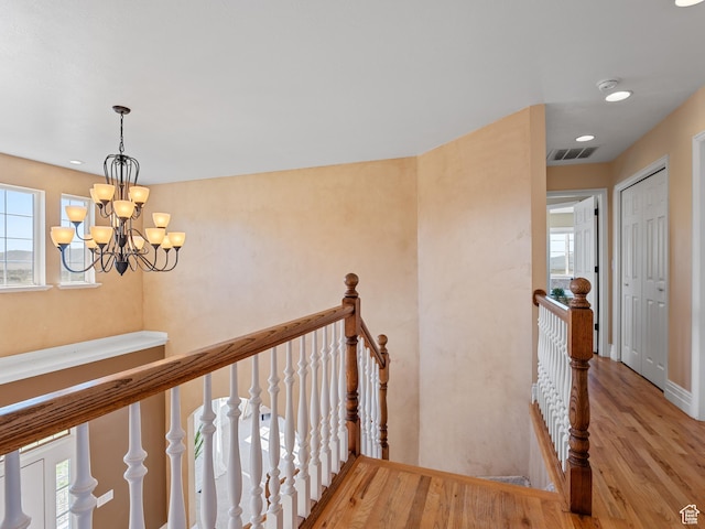 hall with an upstairs landing, wood finished floors, a chandelier, and recessed lighting