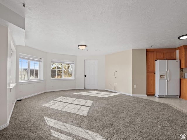 unfurnished living room featuring baseboards, a textured ceiling, and light carpet