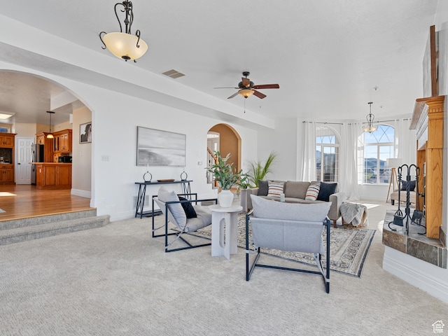 living area featuring light colored carpet, arched walkways, a ceiling fan, and baseboards