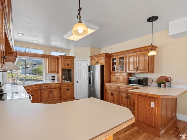 kitchen with appliances with stainless steel finishes, a peninsula, light countertops, light wood finished floors, and glass insert cabinets